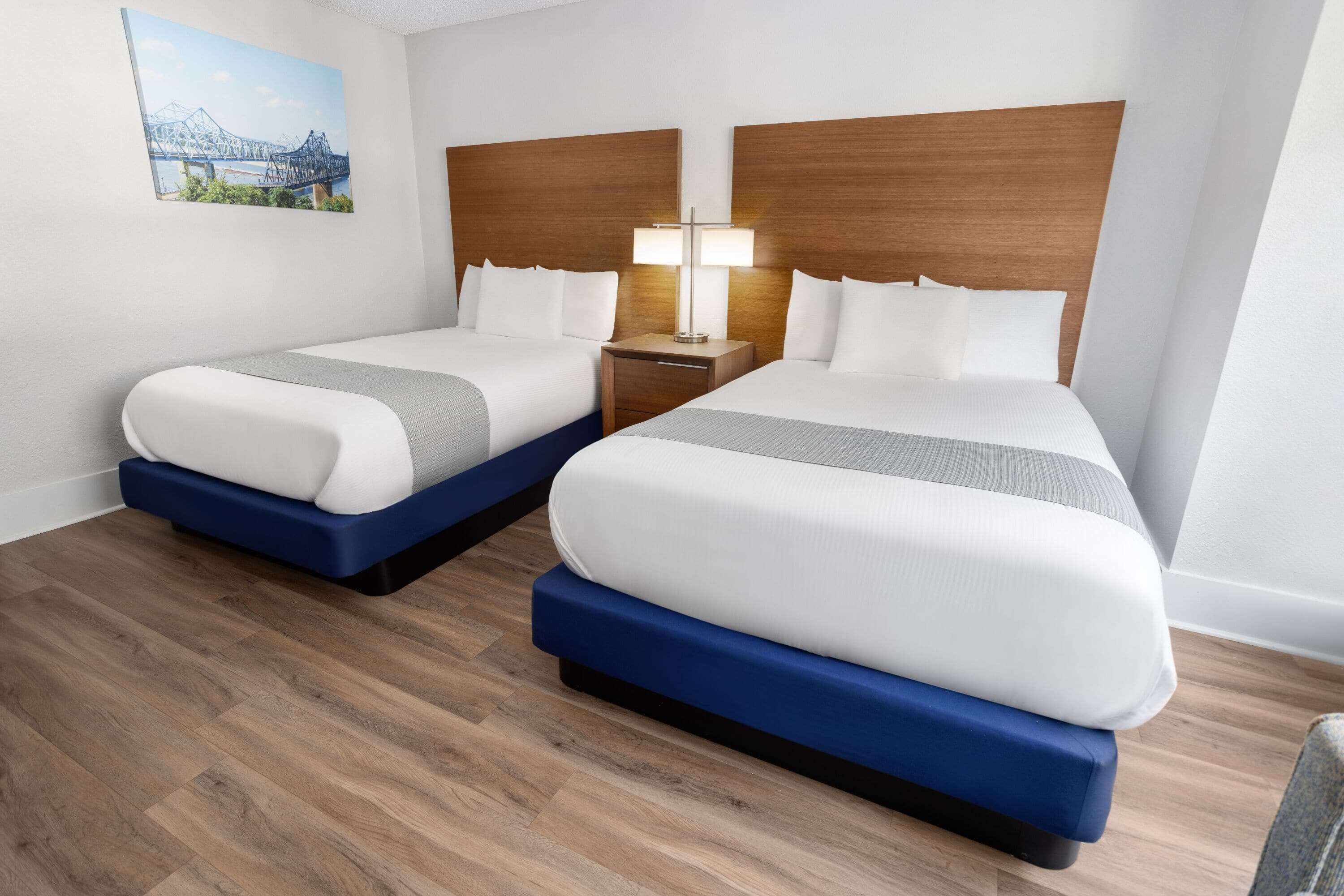 A hotel room with two beds, a nightstand with a lamp, and a painting on the wall.