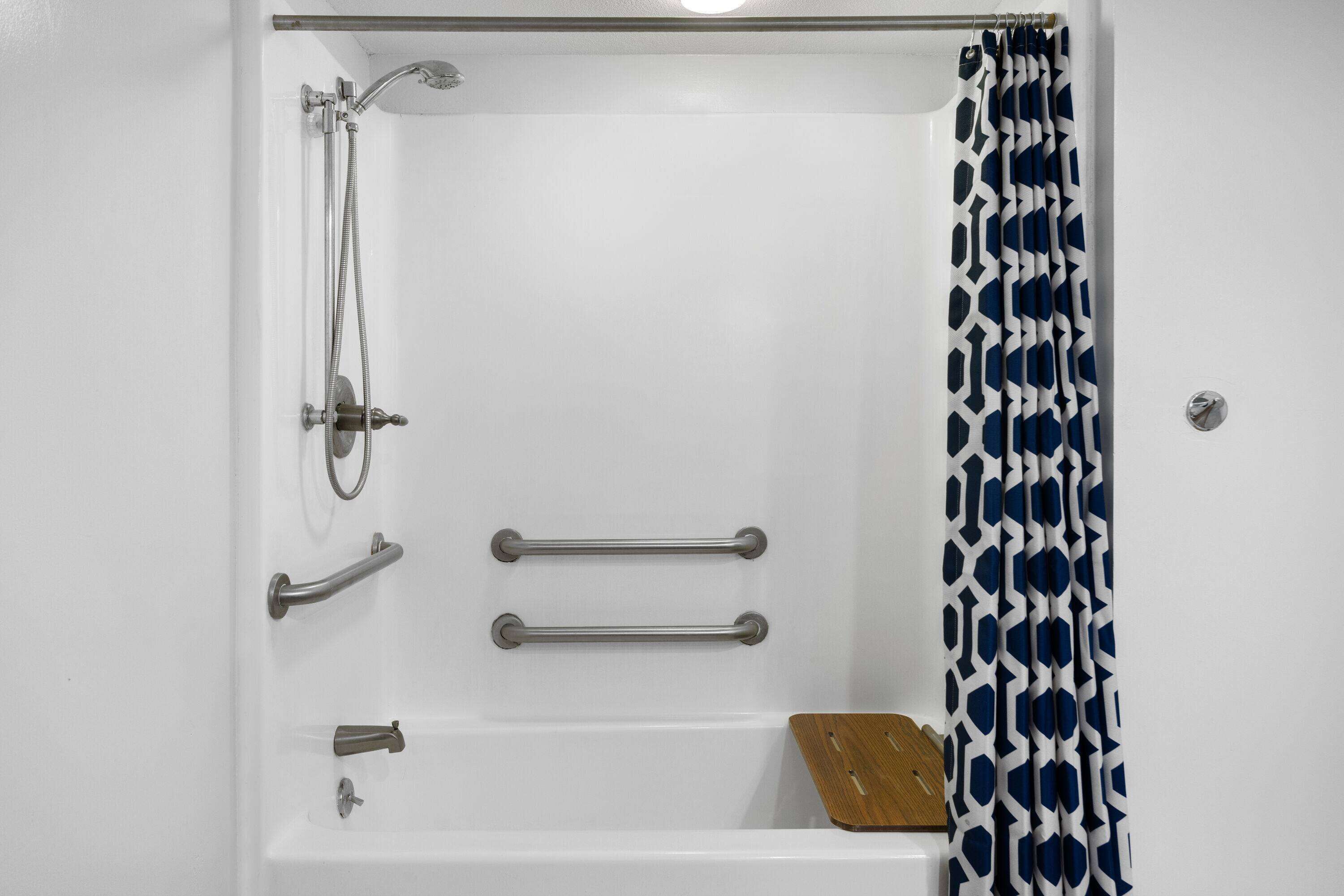 A white bathtub with a showerhead, two grab bars, and a wooden tray.