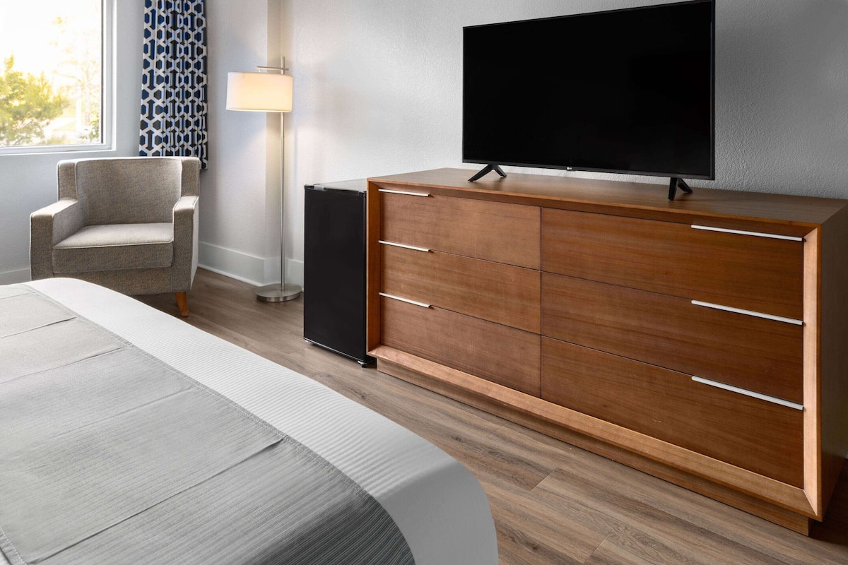 Une chambre d’hôtel moderne avec une commode en bois, un téléviseur à écran plat, une chaise et une lampe.