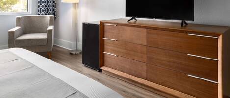 Ein modernes Hotelzimmer mit einem Holzschrank, einem Flachbildfernseher, einem Sessel und einer Lampe.