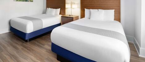 A hotel room with two beds, wooden headboards, a nightstand with a lamp, and a painting on the wall.