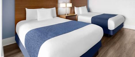Ein Hotelzimmer mit zwei Betten, Holz-Kopfteilen, einem Nachttisch mit Lampe und einem blauen Akzent an den Betten.