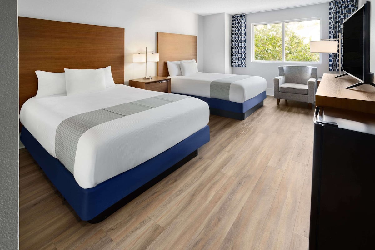 A hotel room with two beds, a TV, a desk, and a chair.