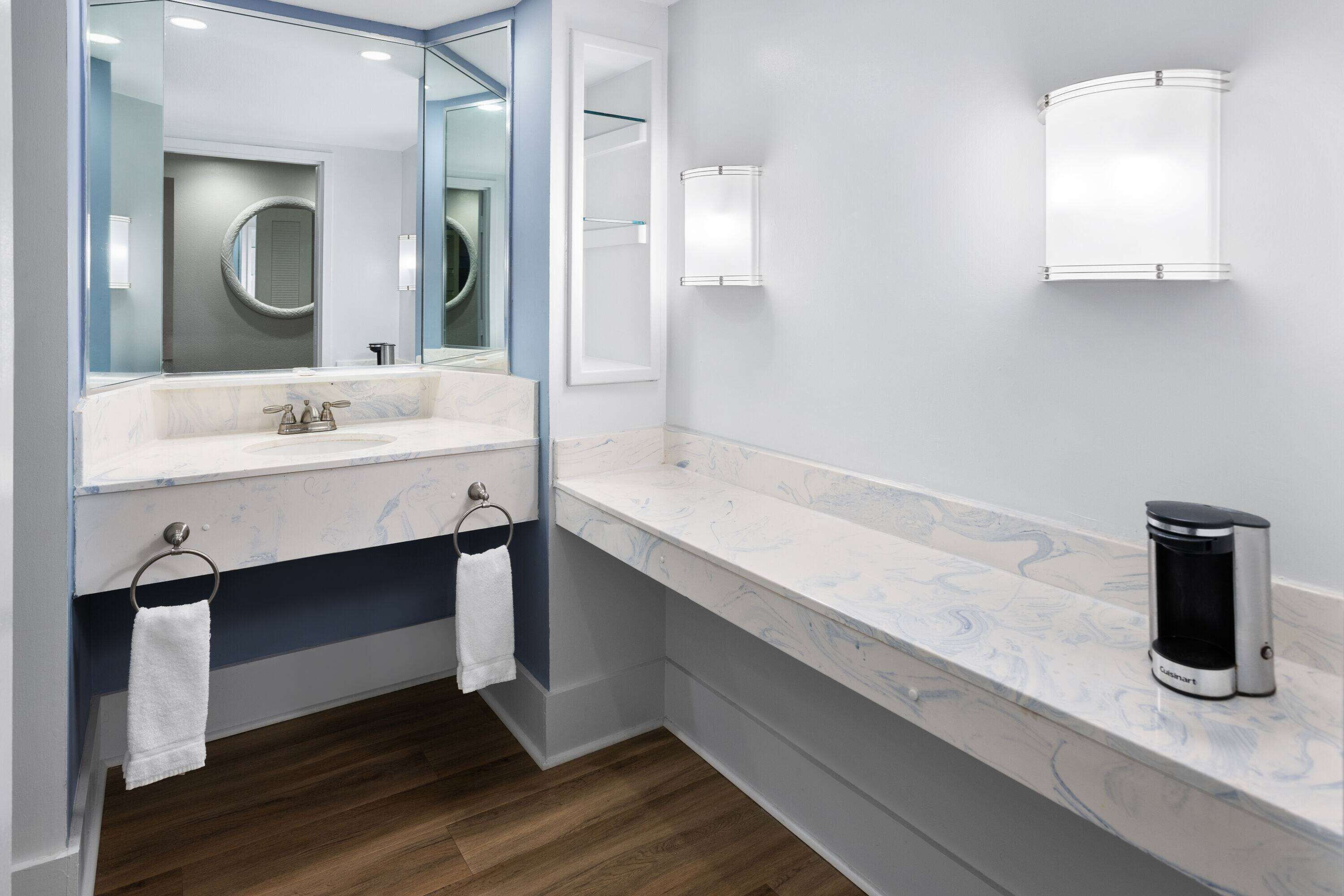 A modern bathroom with a marble countertop, a sink, a mirror, and a coffee maker.