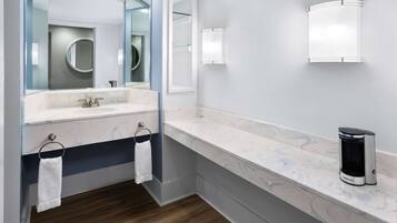 A modern bathroom with a marble countertop, a sink, a mirror, and a coffee maker.