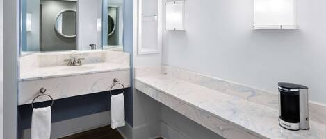 Un bagno moderno con piano in marmo, lavabo, specchio e macchina da caffè.
