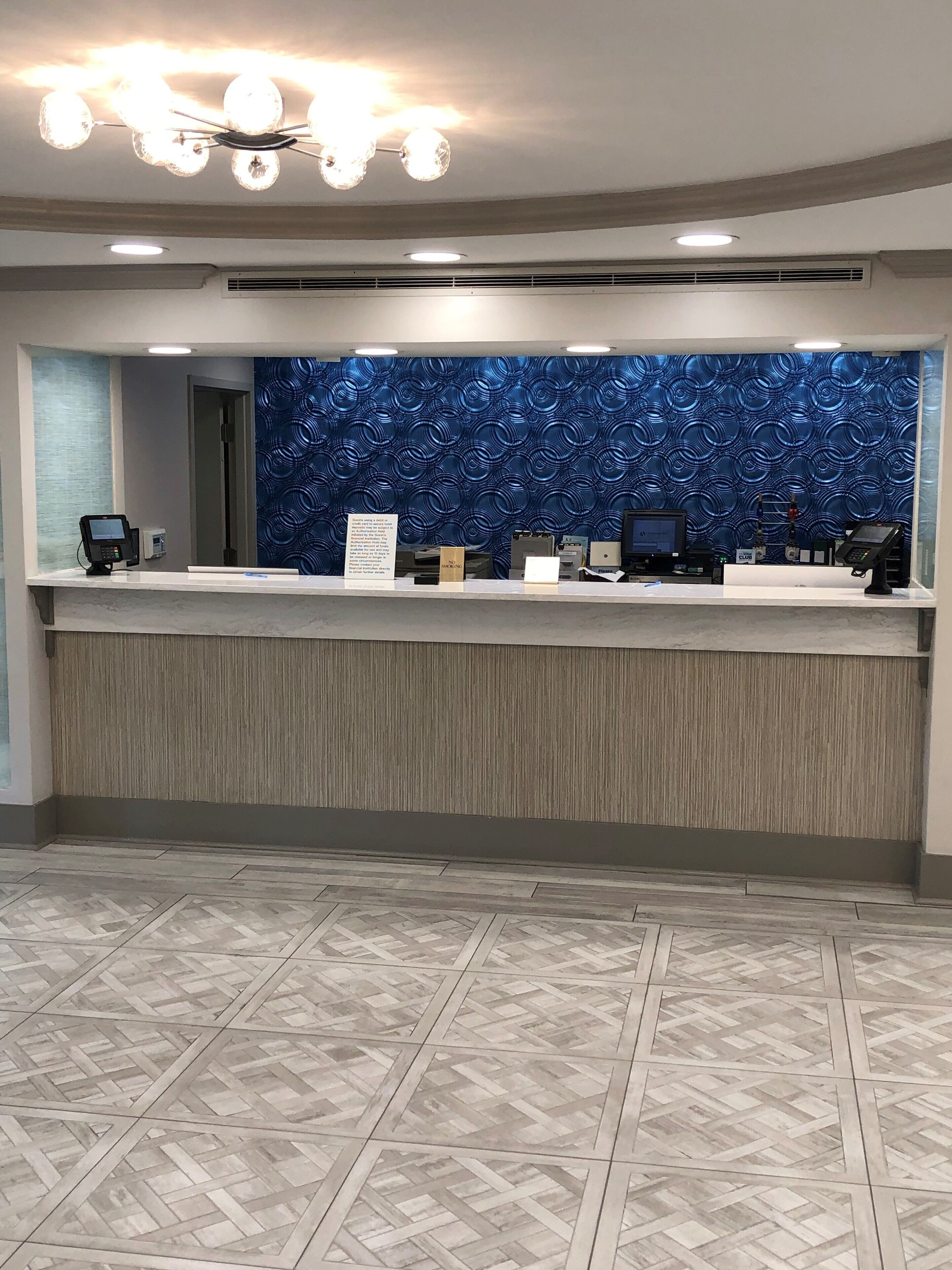 Un espace d’accueil au design moderne, avec un mur bleu à motifs, un comptoir en marbre et un plafond agrémenté d’un lustre.