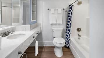 A bathroom with a white toilet, a bathtub, a shower curtain, and a sink with a mirror.