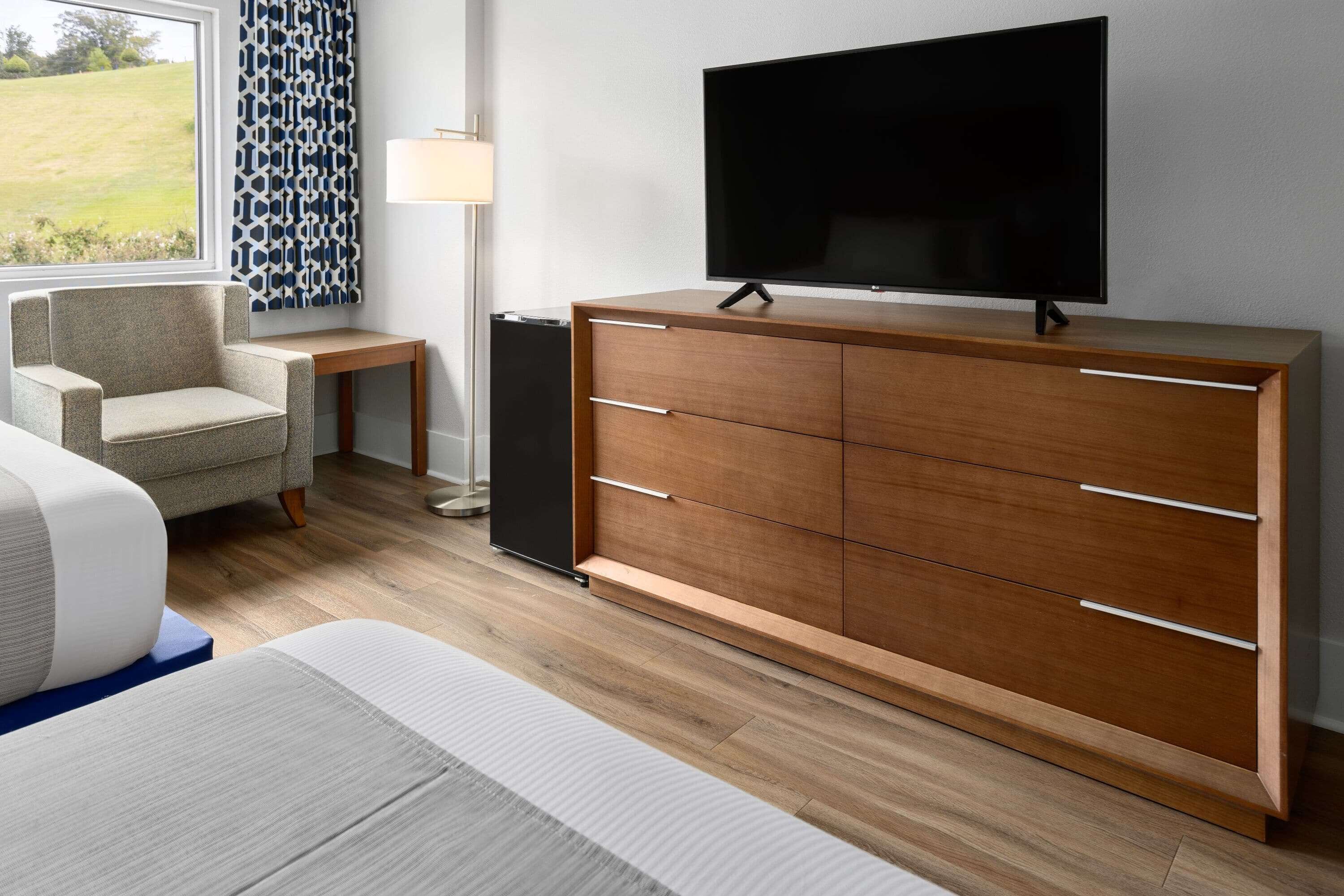 A modern room with a wooden cabinet, a flat-screen TV, a sofa, and a patterned curtain.