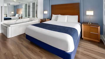 A modern hotel room with a large bed, a separate bathroom area, a wooden headboard, bedside lamps, and a large mirror.
