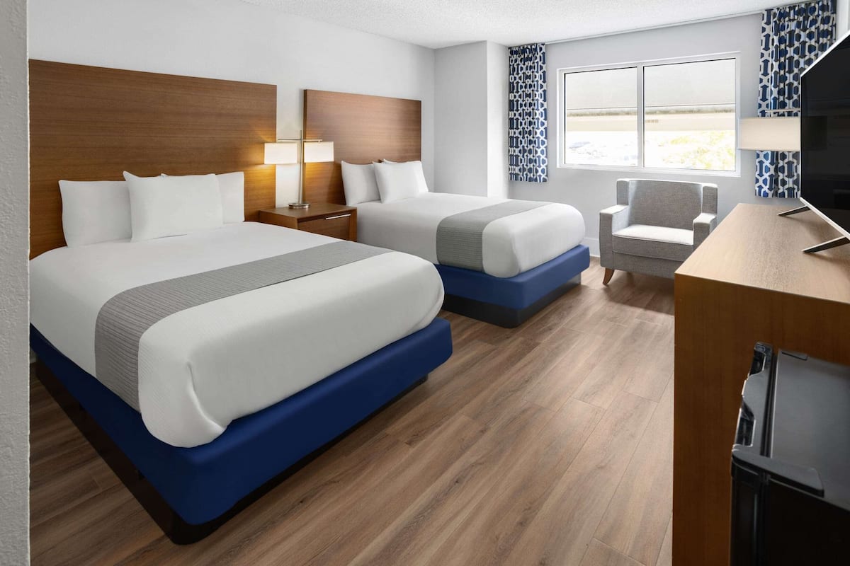 A hotel room with two beds, a desk, a chair, a TV, and a window with a view.