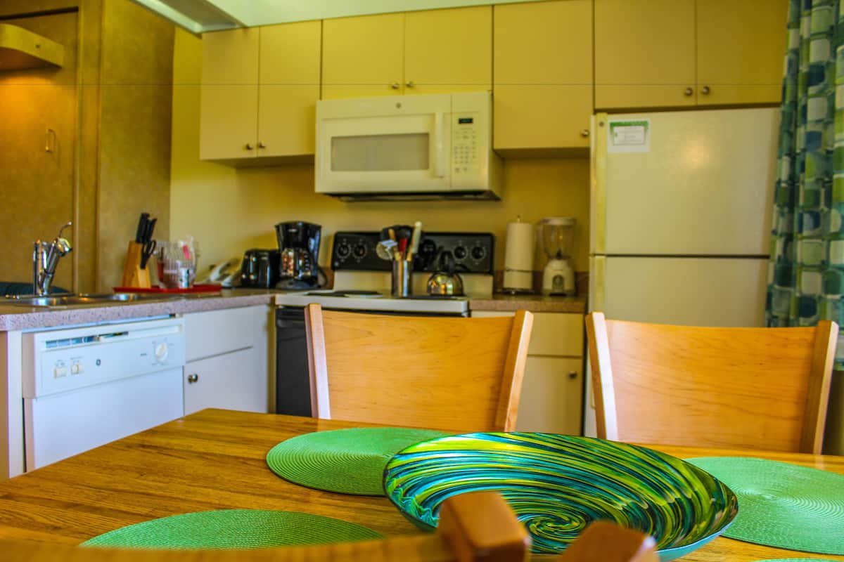 Een keuken met houten kastjes, een magnetron, een koelkast en een eettafel met stoelen.
