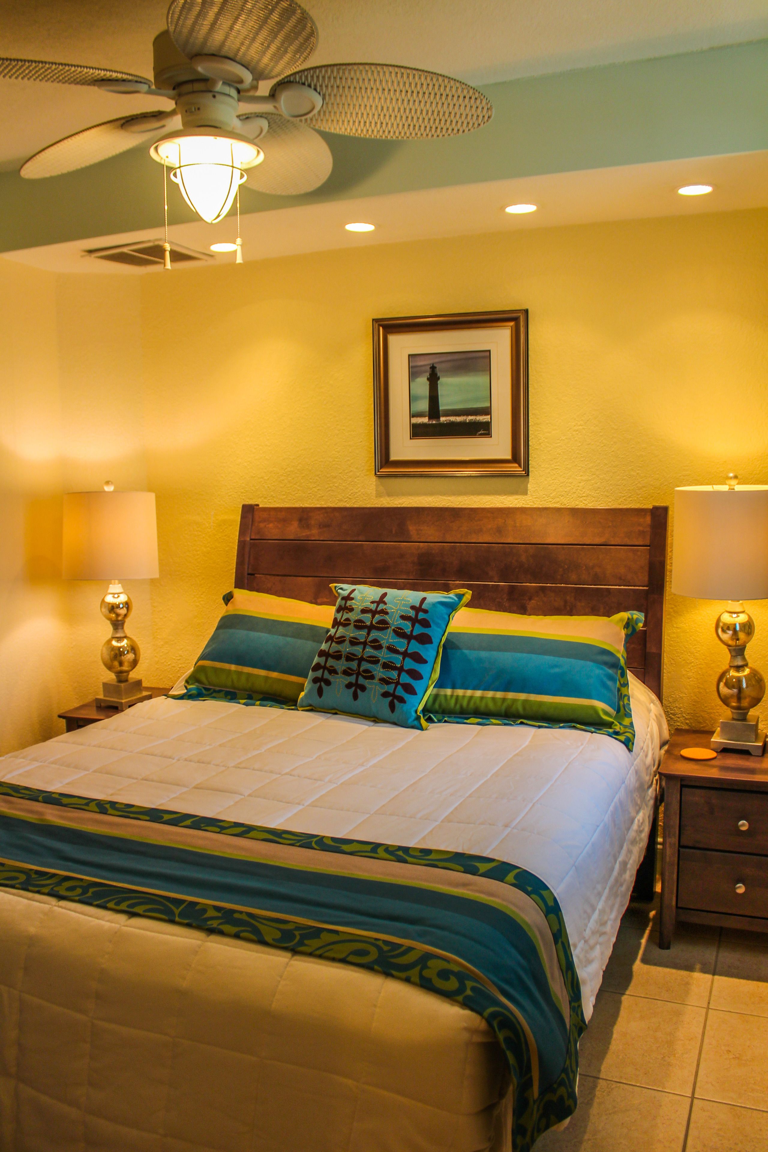 A bedroom with a bed, nightstands, a ceiling fan, and a framed picture on the wall.