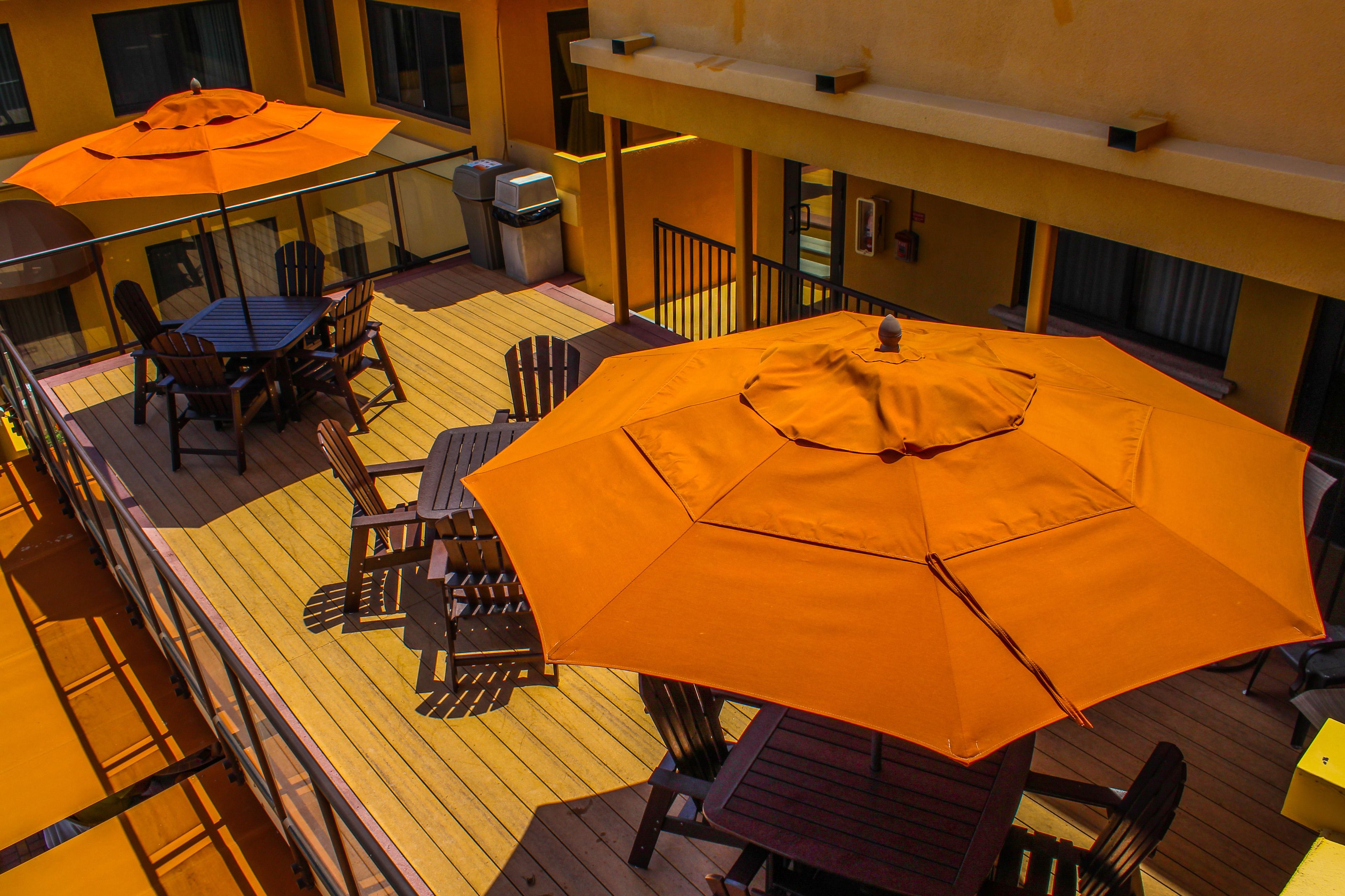 Una terrazza esterna con pavimento in legno, due tavoli con ombrelloni arancioni e diversi posti a sedere.