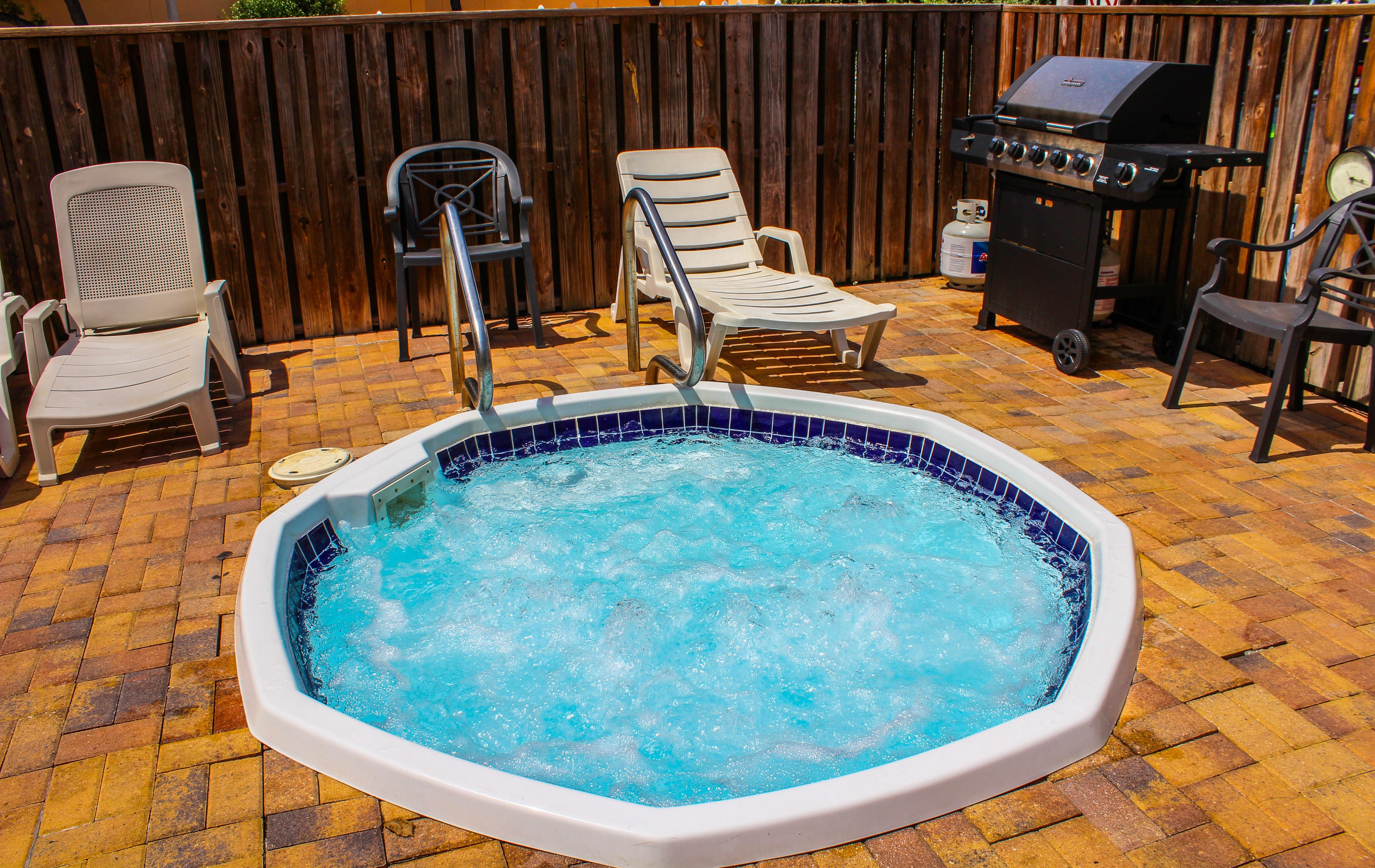 A hot tub surrounded by patio chairs and a barbecue grill.