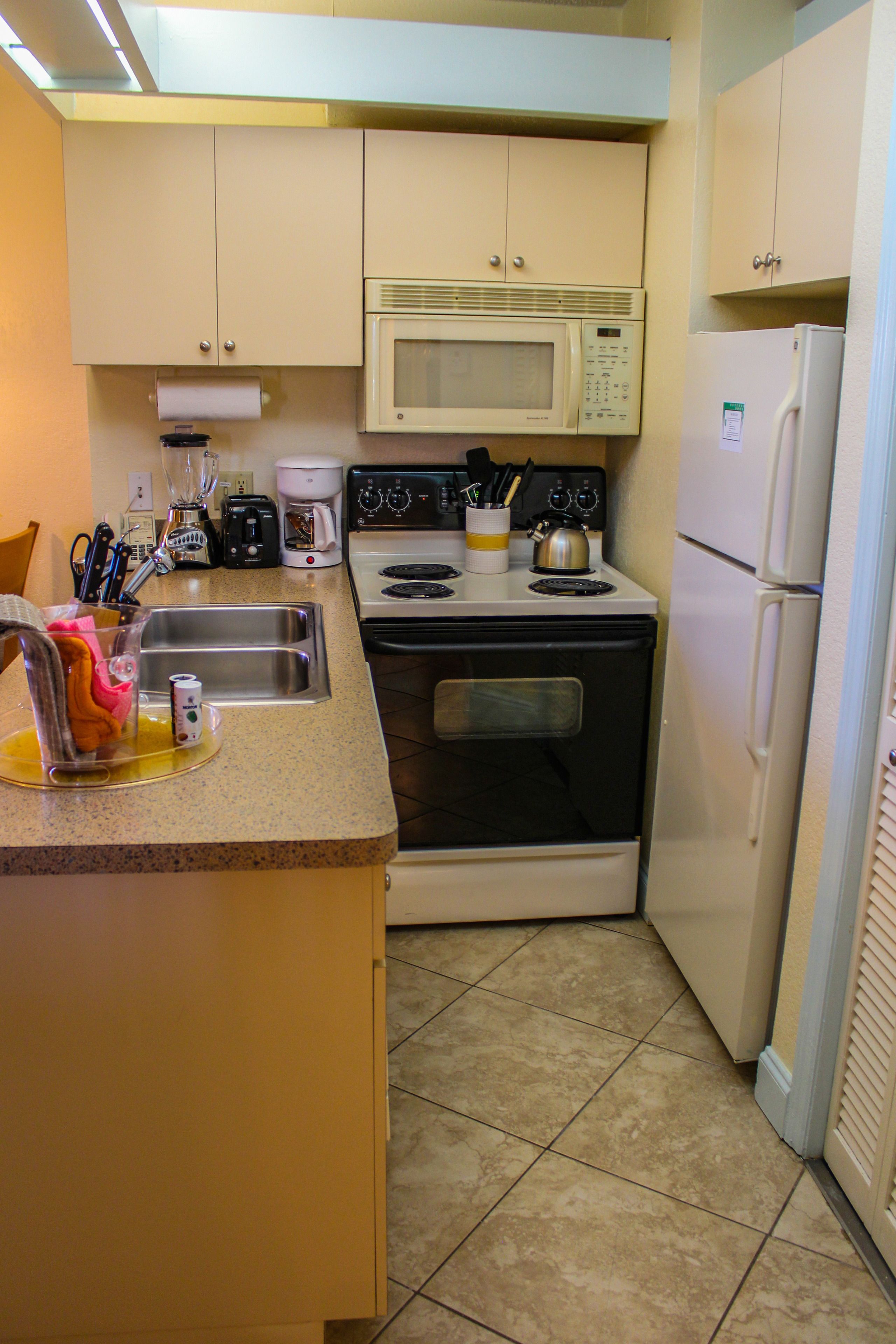 A compact kitchen with a sink, stove, microwave, and refrigerator.