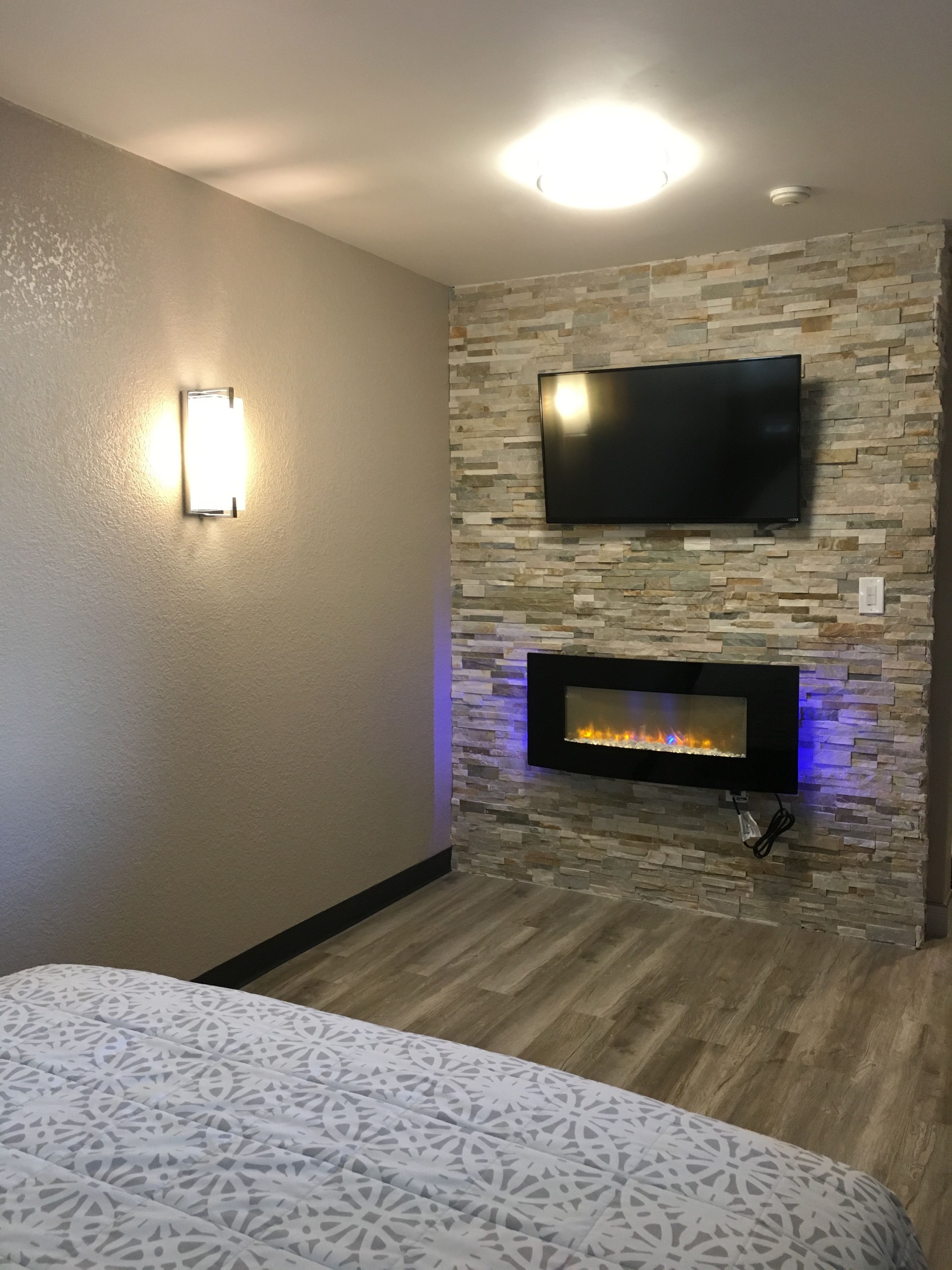 Una habitación con una televisión de pantalla plana montada en una pared de piedra, una chimenea encendida y una colcha de diseño.
