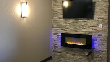 Una habitación con una televisión de pantalla plana montada en una pared de piedra, una chimenea encendida y una colcha de diseño.