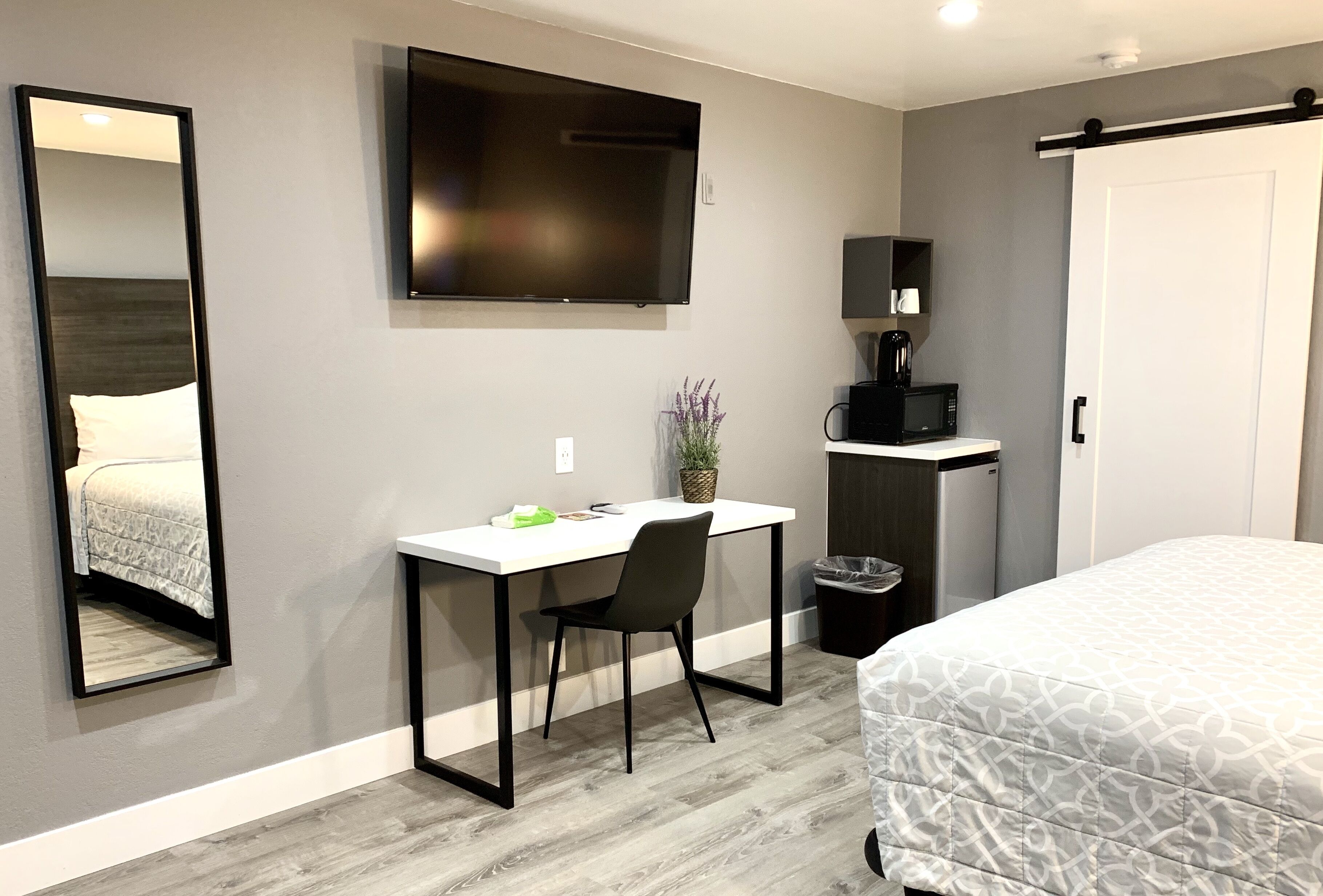 Una habitación de hotel con cama, escritorio con silla, televisor, cafetera y cubo de basura.