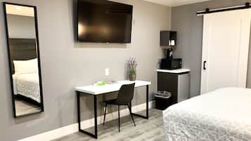Una habitación de hotel con cama, escritorio con silla, televisor, cafetera y cubo de basura.