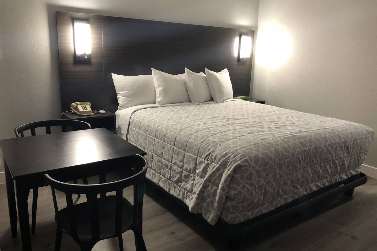 A hotel room with a bed, bedside table, chair, and a desk with a telephone.