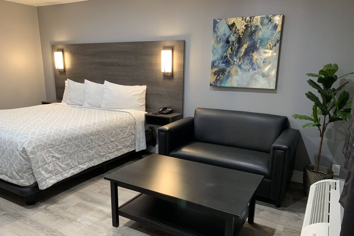 A modern hotel room with a bed, a black leather sofa, a coffee table, and a wall-mounted air conditioner.