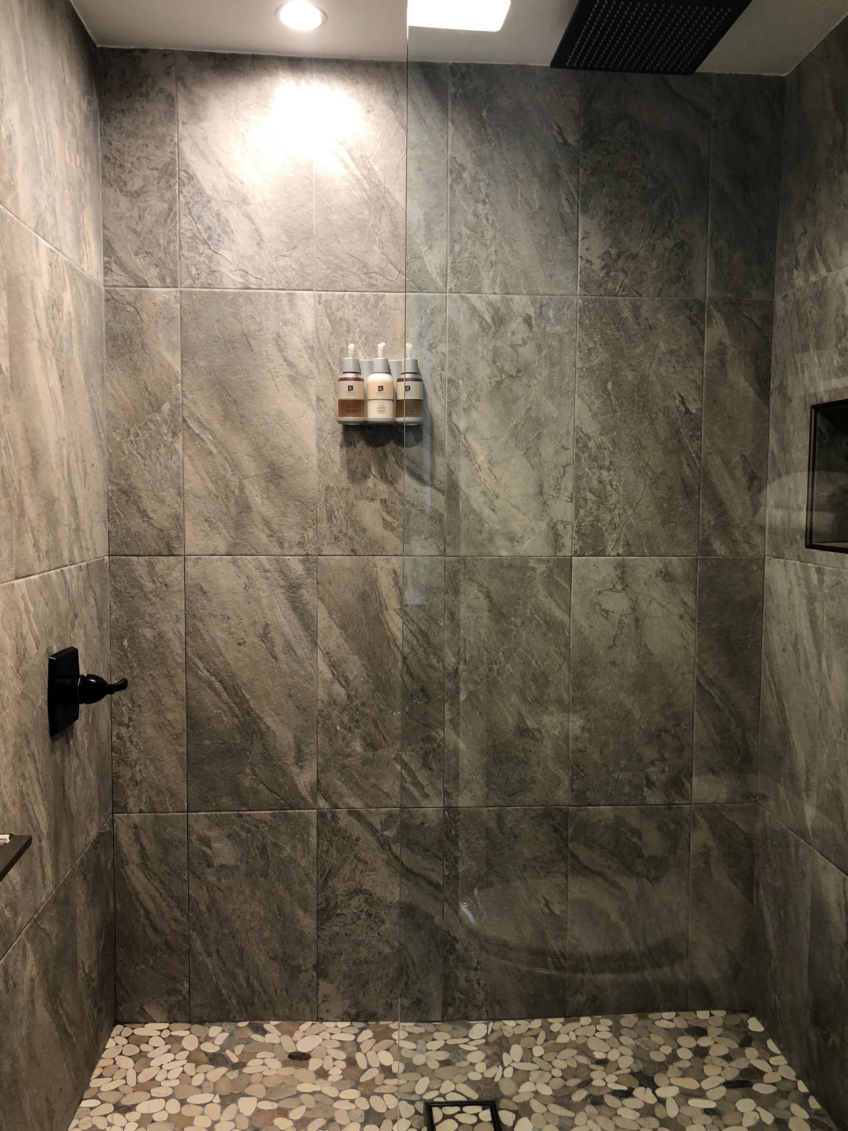 A shower with a tiled wall and a pebble-patterned floor.