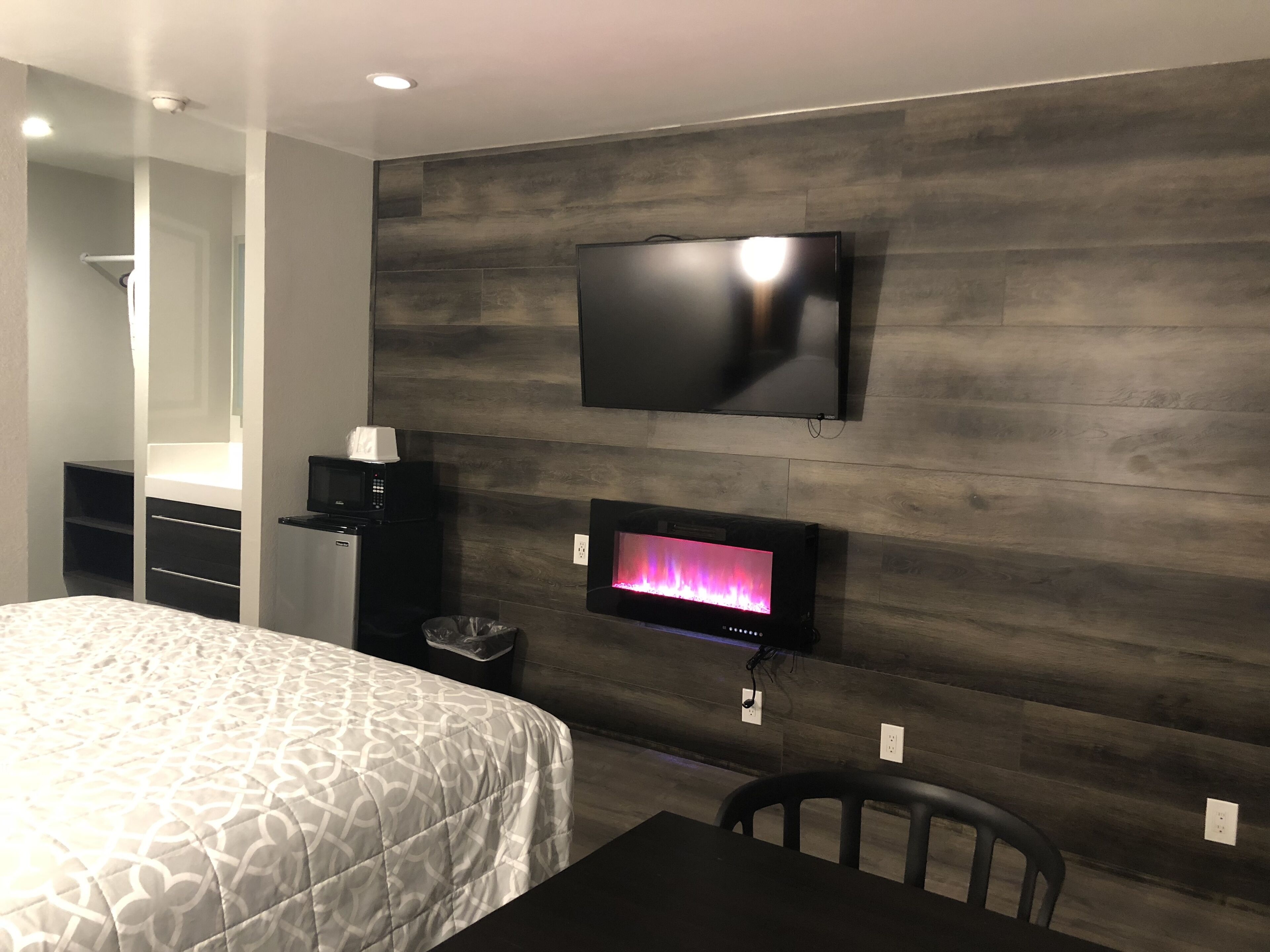 Una habitación de hotel moderna con una cama grande, un televisor de pantalla plana en la pared, una pequeña chimenea y un escritorio con una silla.