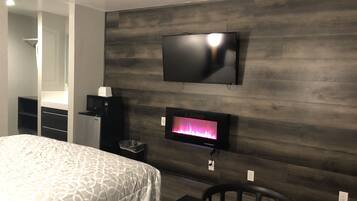Una habitación de hotel moderna con una cama grande, un televisor de pantalla plana en la pared, una pequeña chimenea y un escritorio con una silla.