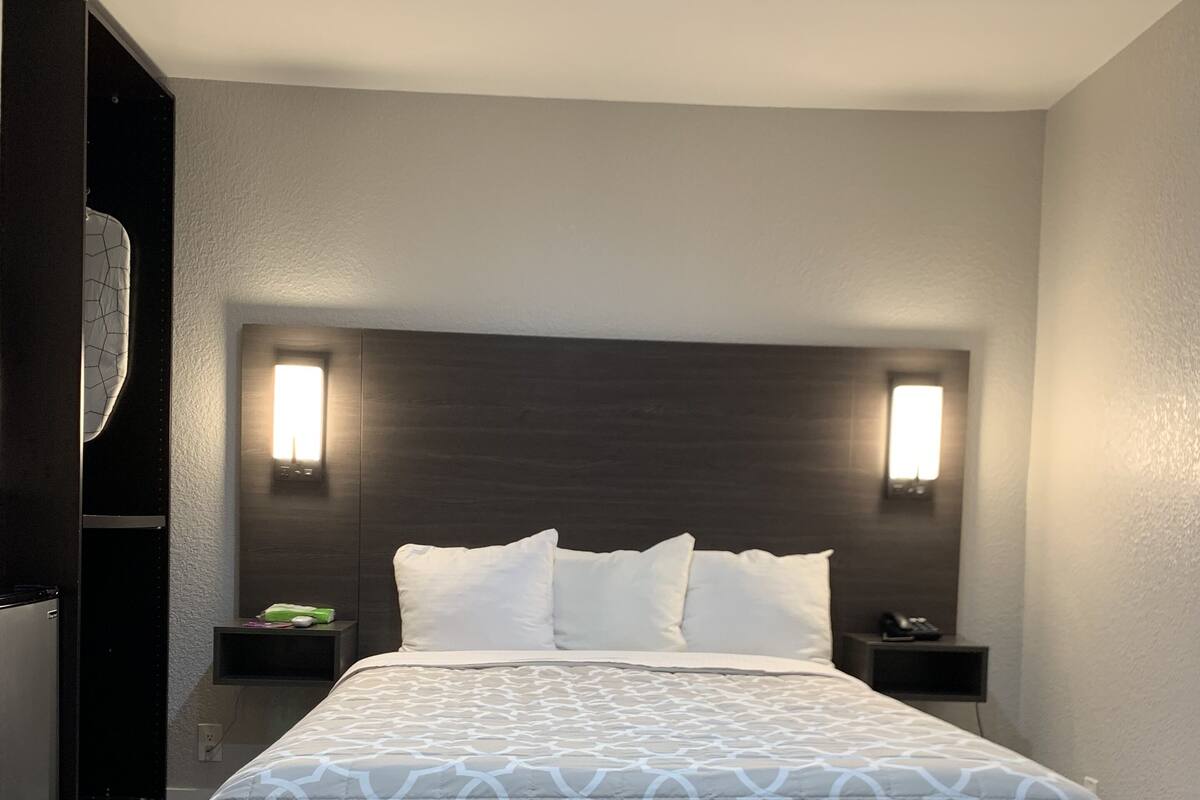 A modern hotel room with a large bed, two bedside tables, a dark headboard, and a light-colored wall.