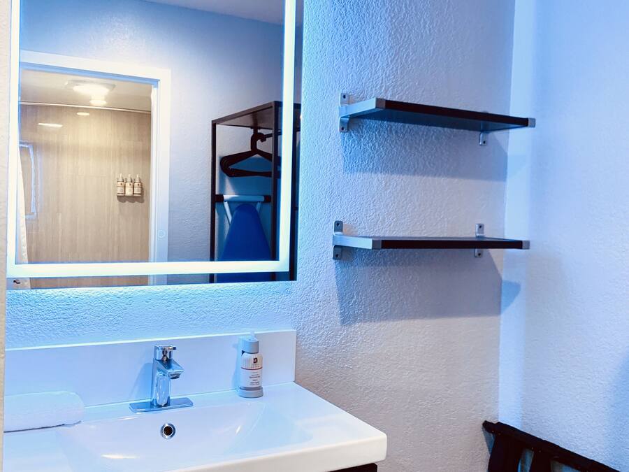 A modern bathroom with a large mirror, a white sink, and a towel rack.