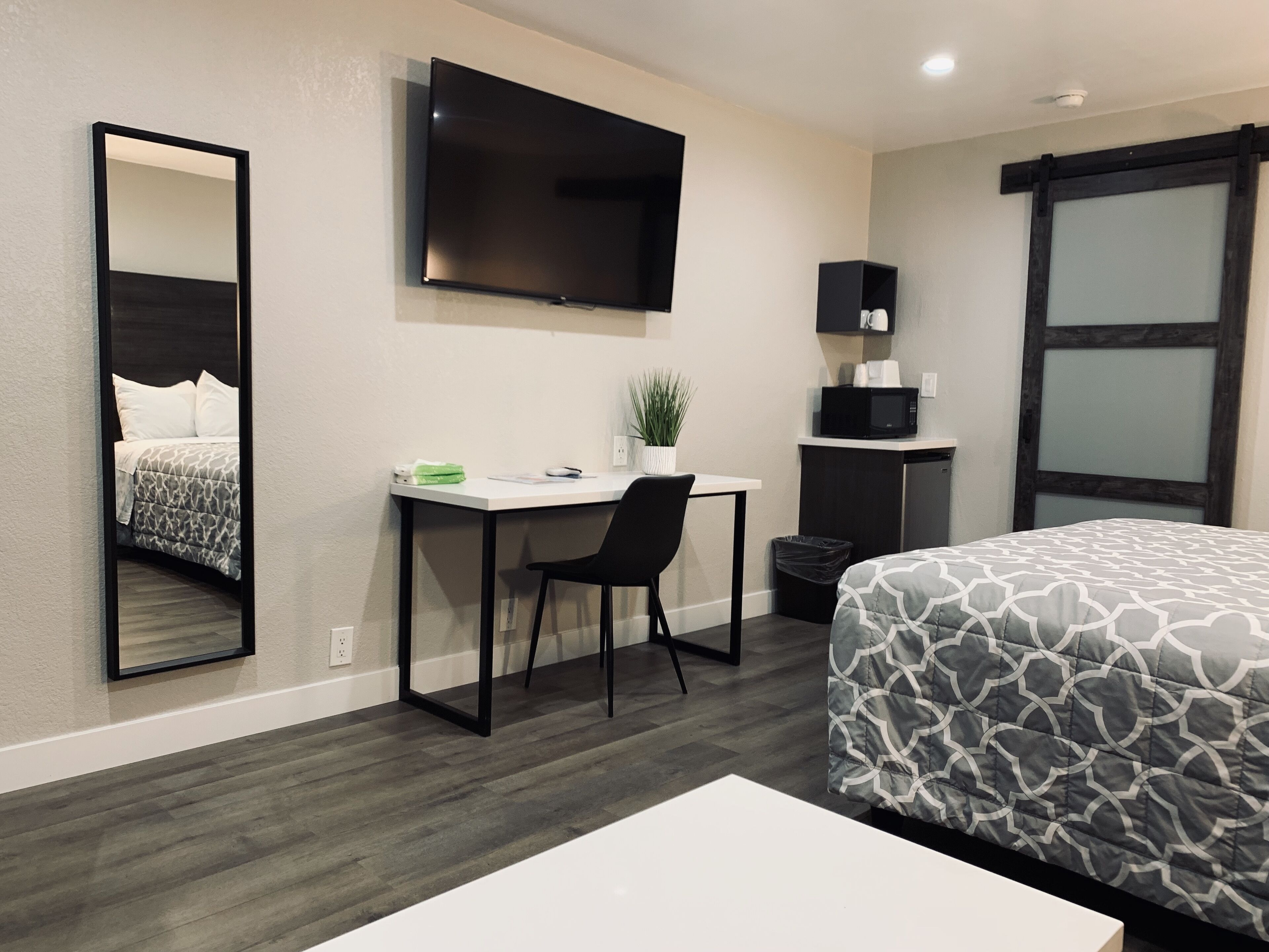 A hotel room with a bed, a desk, a chair, a TV, a microwave, and a trash bin.