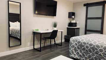 A hotel room with a bed, a desk, a chair, a TV, a microwave, and a trash bin.