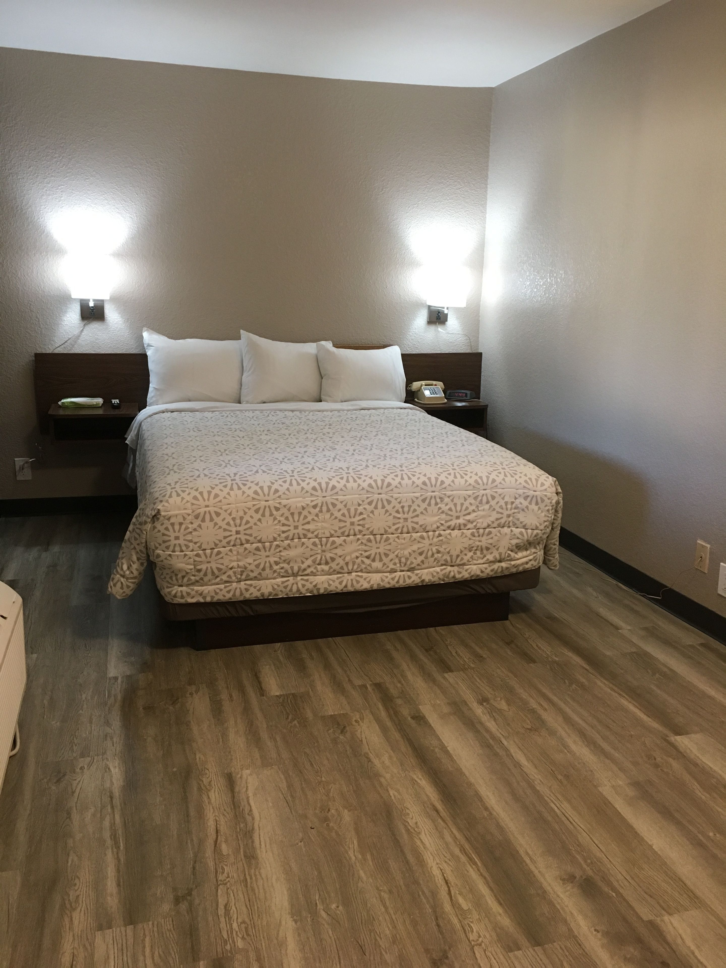 Une chambre d’hôtel bien aménagée, avec un grand lit, deux tables de chevet, une petite table et un téléphone fixé au mur.