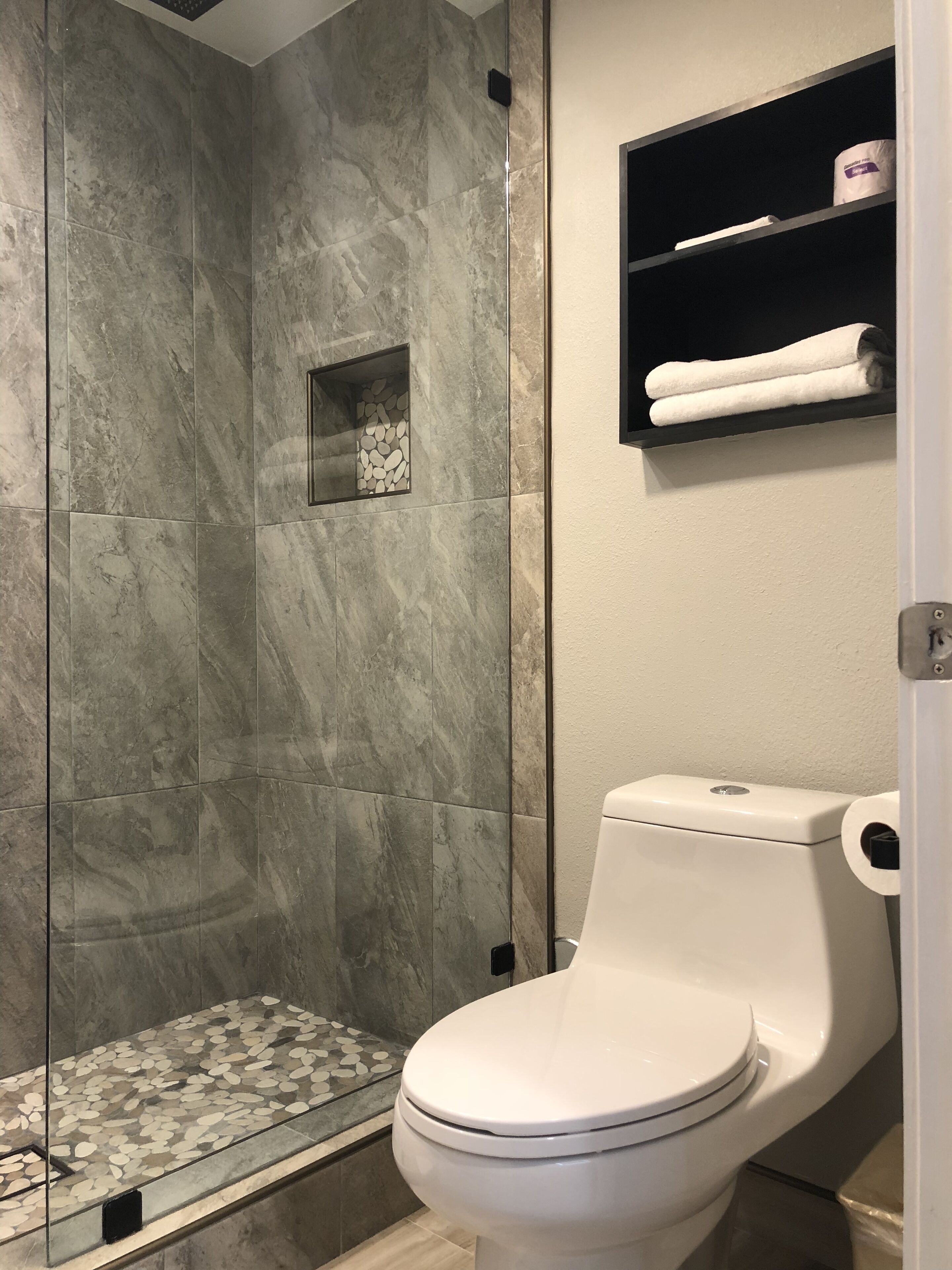 A bathroom with a glass-enclosed shower, a toilet, and a shelf with towels.