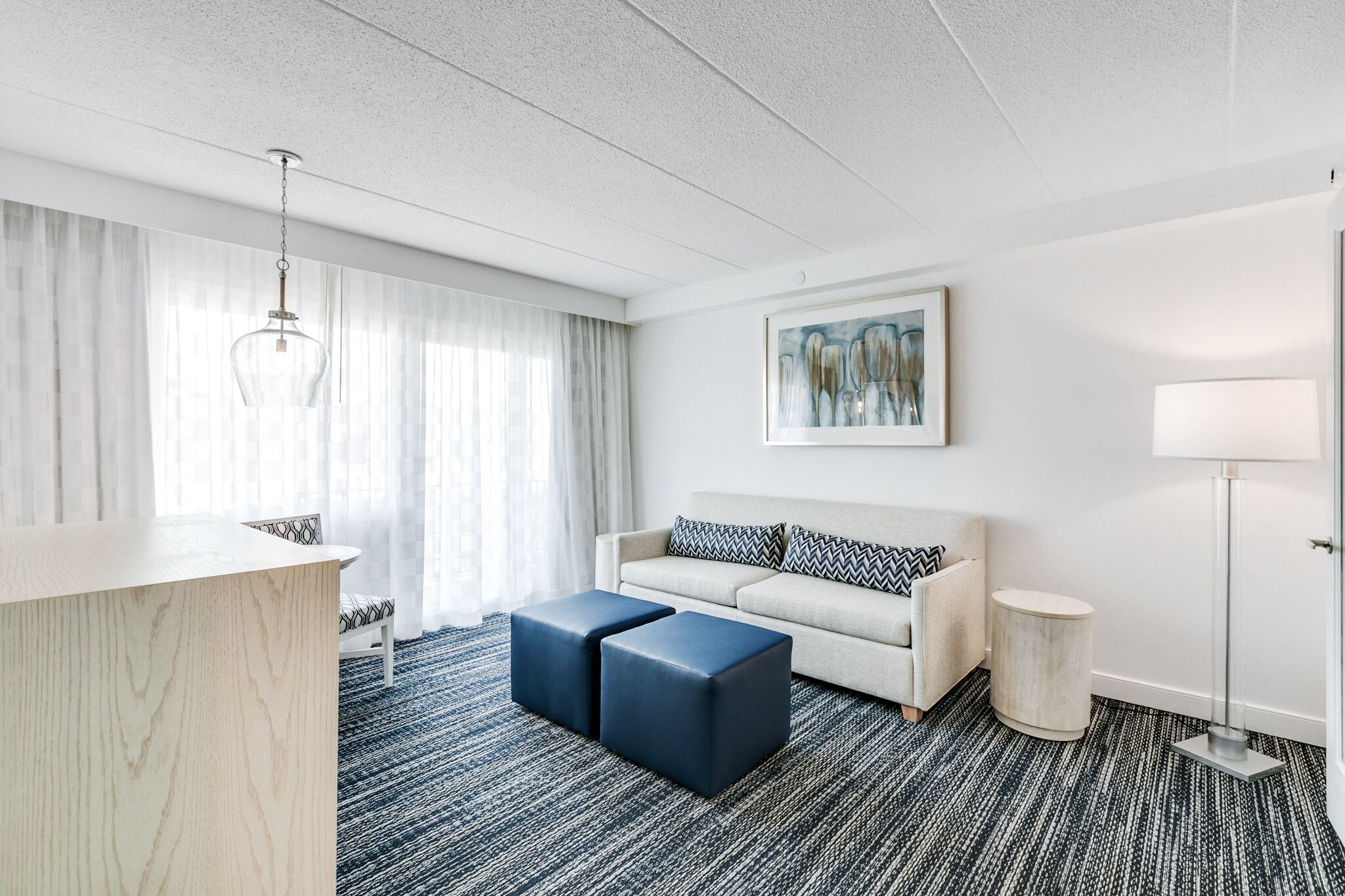 Una habitación de hotel moderna con un ventanal grande, un sofá, una mesa de centro, un escritorio y una lámpara.
