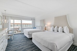 A hotel room with two beds, a dresser, a desk, and a large window with a view of buildings. - ICONA Windrift (Avalon)