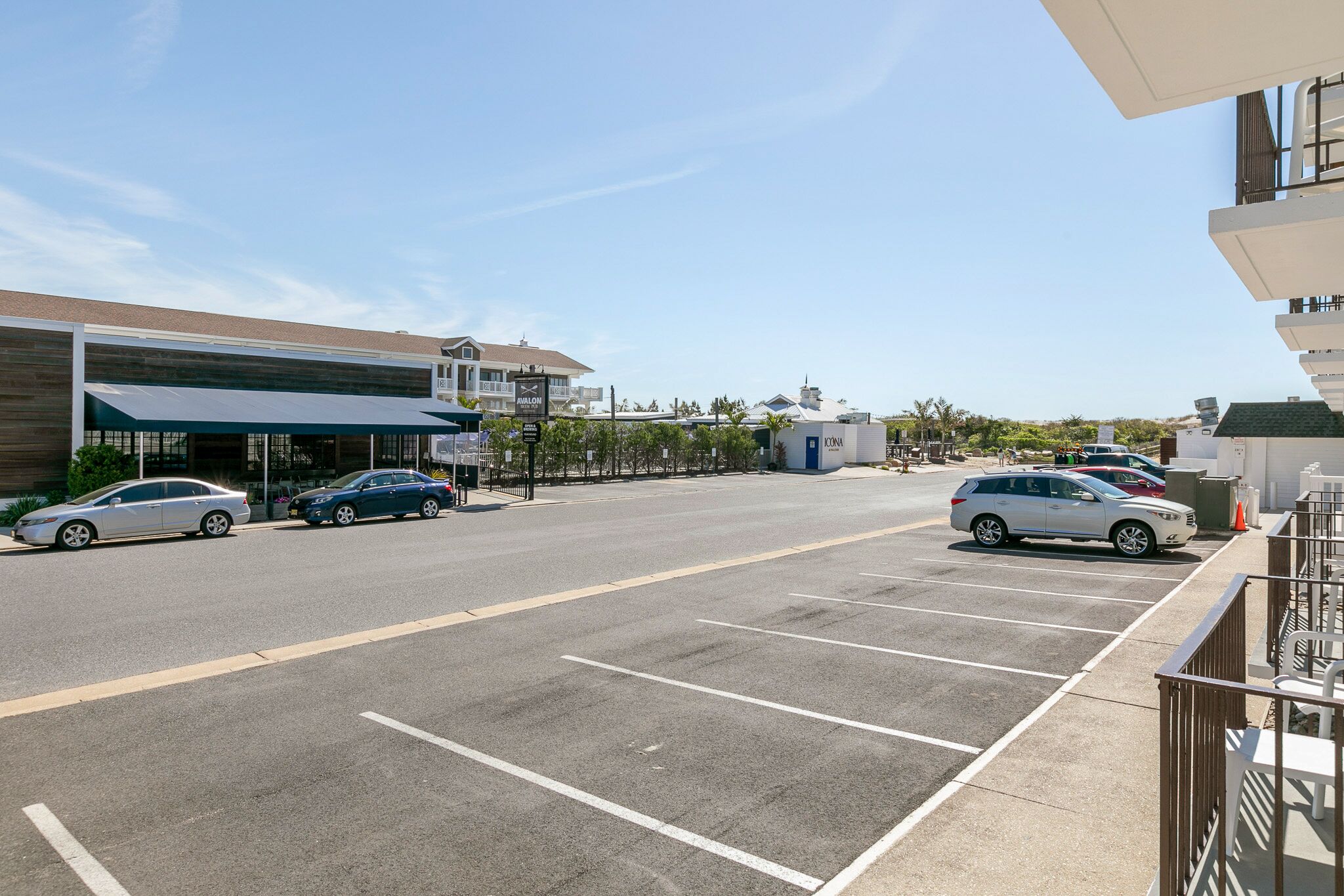 A parking lot with several cars, a building with a sign that reads "CONIA," and a clear blue sky.