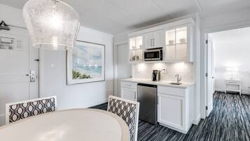 A modern kitchen with white cabinets, a microwave, and a dishwasher. There is a dining area with a table and chairs.