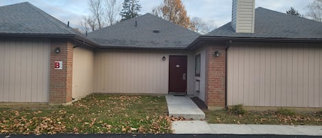 A two-story building with a dark roof, beige siding, and a red front door.