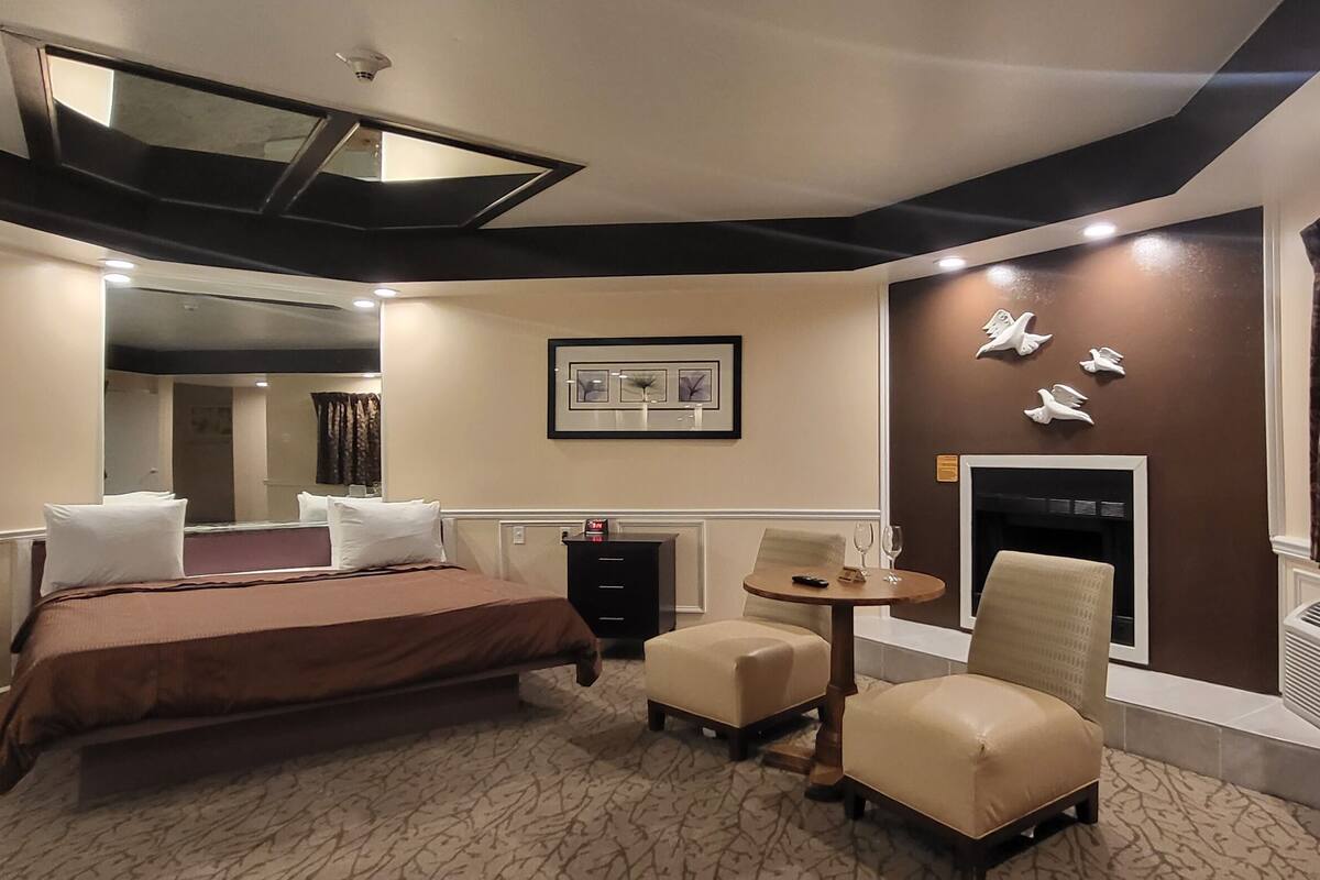 A hotel room with a large bed, a small round table, two chairs, a fireplace, and a ceiling skylight.
