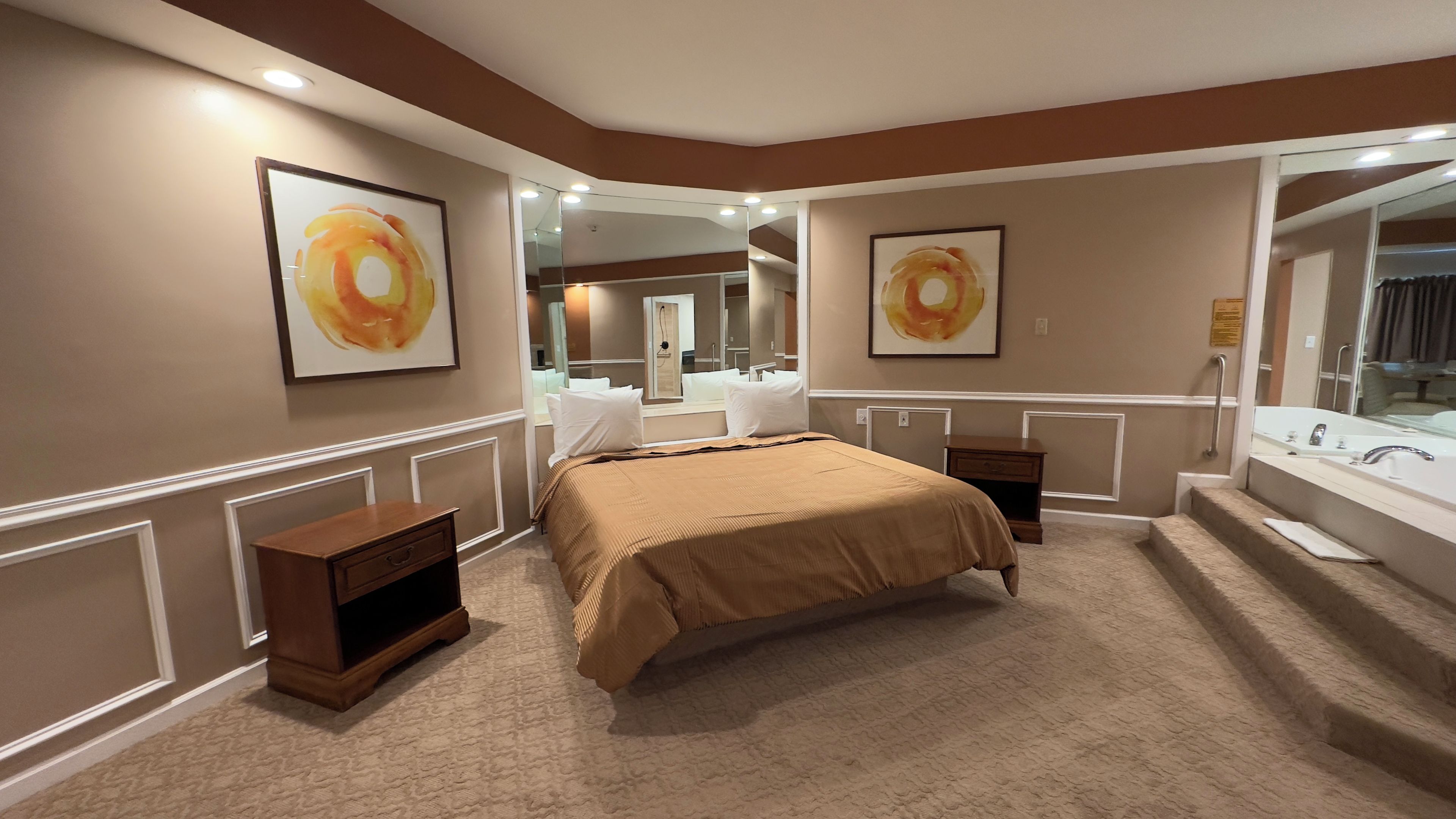 A hotel room with a large bed, a bedside table, a nightstand, a mirror, and a bathroom with a sink and mirror.