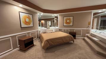 A hotel room with a large bed, a bedside table, a nightstand, a mirror, and a bathroom with a sink and mirror.