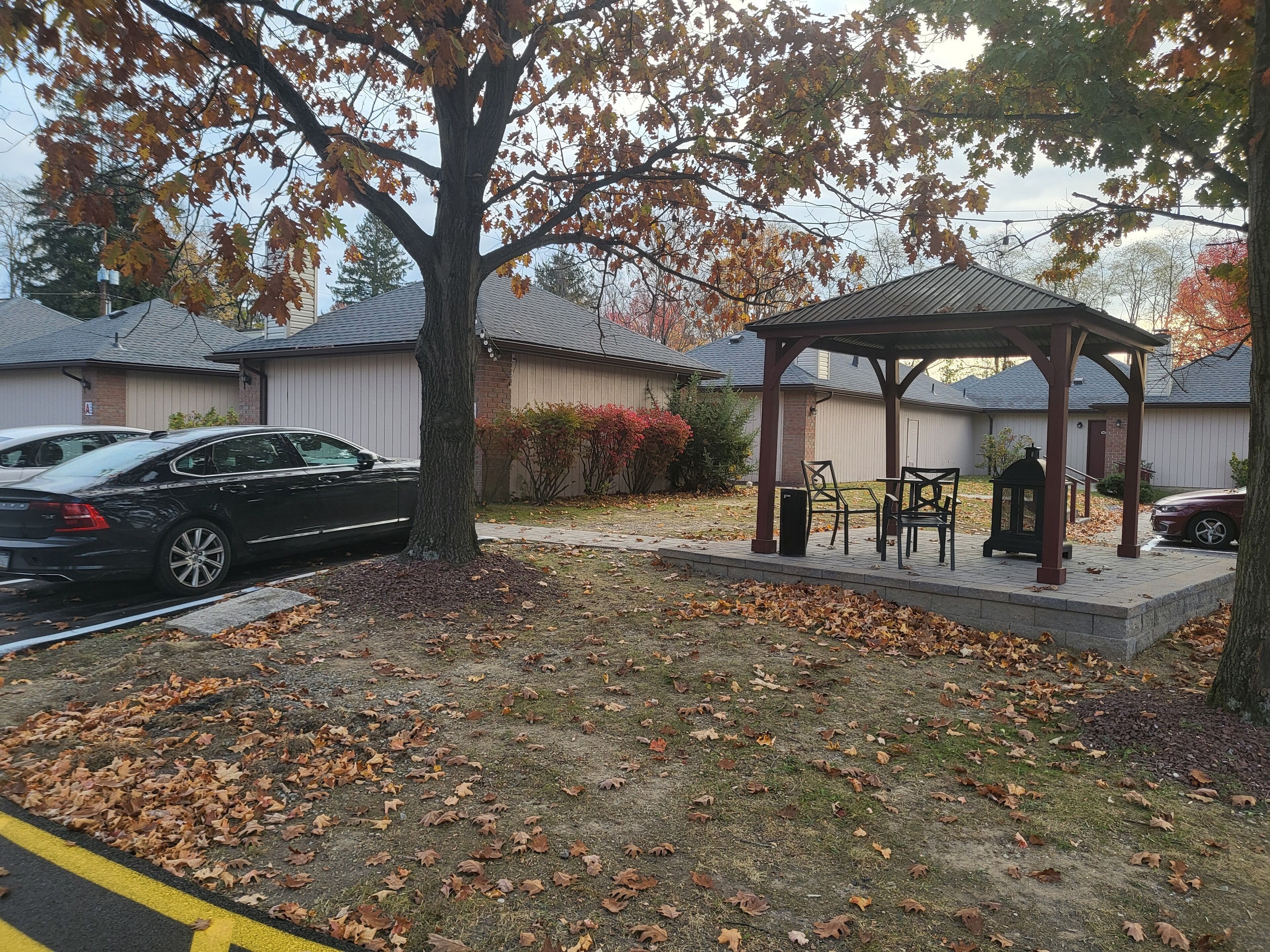 A gazebo with chairs and a table, surrounded by a grassy area with fallen leaves.