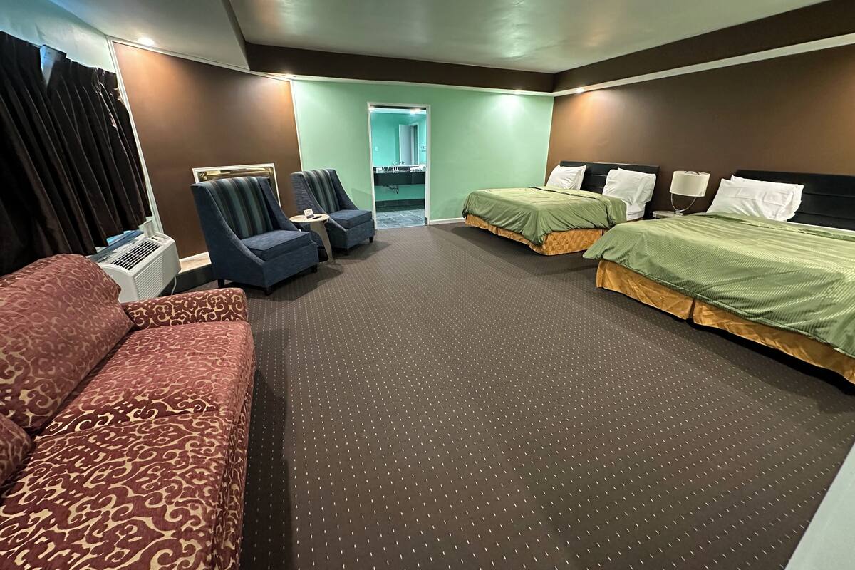 A hotel room with two single beds, a sofa, two armchairs, a small table, and a mirror.