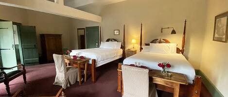 A hotel room with two beds, a wooden chair, a small table, and a desk.