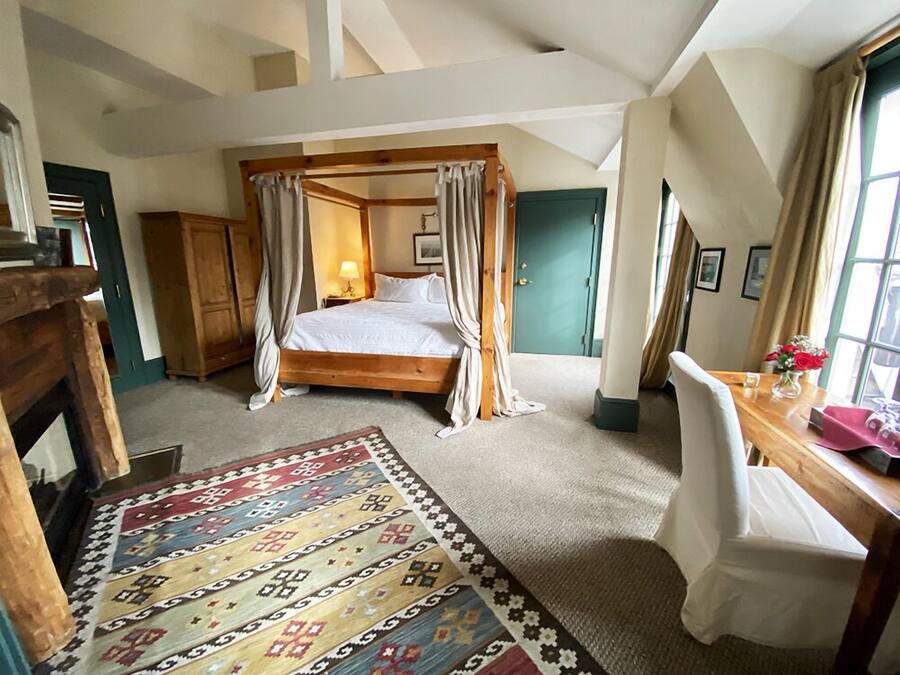 A bedroom with a four-poster bed, a wooden desk with a vase of flowers, a patterned rug, and a green door.