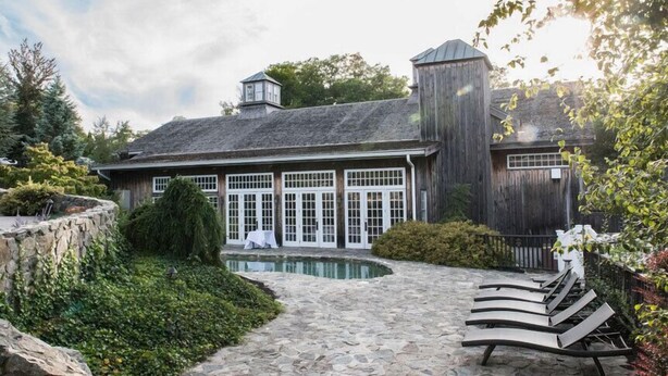 A building with a stone pathway leading to a pool area, surrounded by greenery and a wooden fence. - The Red Lion Inn Resort 1704 (Cohasset)