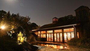 A rustic building with large windows and a wooden exterior, surrounded by trees and a reflective water feature. - The Red Lion Inn Resort 1704 (Cohasset)