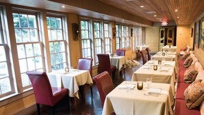 A restaurant with multiple tables and chairs, large windows, and a wooden ceiling. - The Red Lion Inn Resort 1704 (Cohasset)